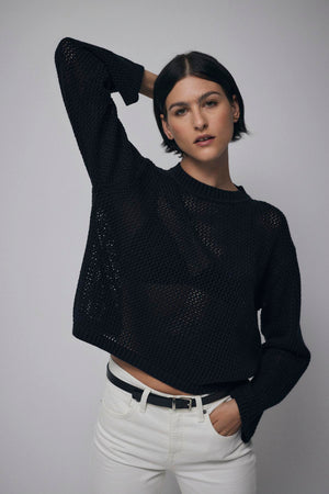 A short-haired person in the KANAN COTTON CASHMERE MESH SWEATER by Velvet by Jenny Graham, styled with white pants, poses against a neutral background with one hand behind their head.
