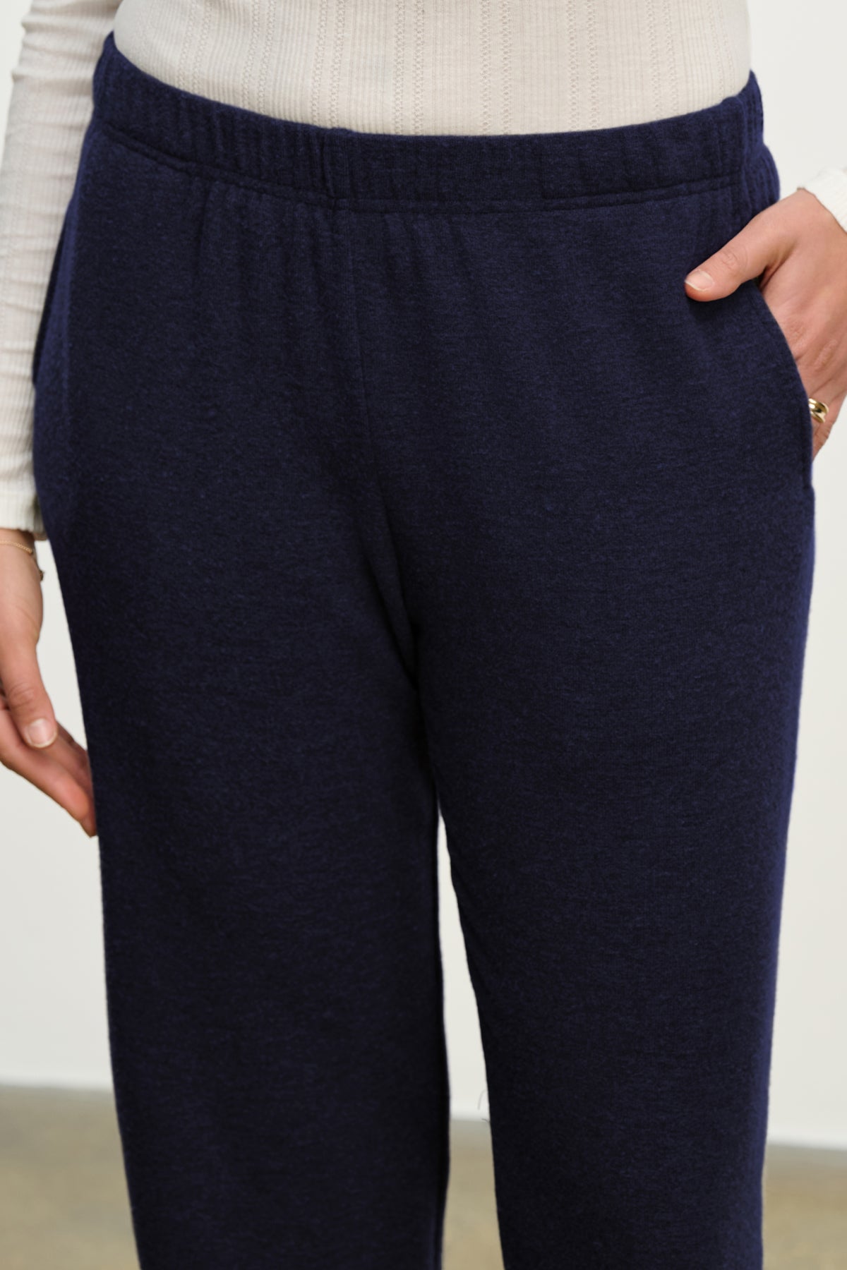 A person wearing a white ribbed long-sleeve top and Velvet by Graham & Spencer’s LEXIE SWEATPANT in navy blue cotton-viscose blend with an elastic waistband, hands in the pockets.-39838381146305