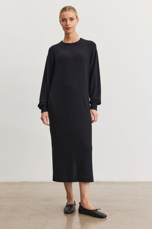 A woman models the AIDA DRESS by Velvet by Graham & Spencer, featuring side seam pockets and a crew neckline, paired with black ballet flats against a plain white background.