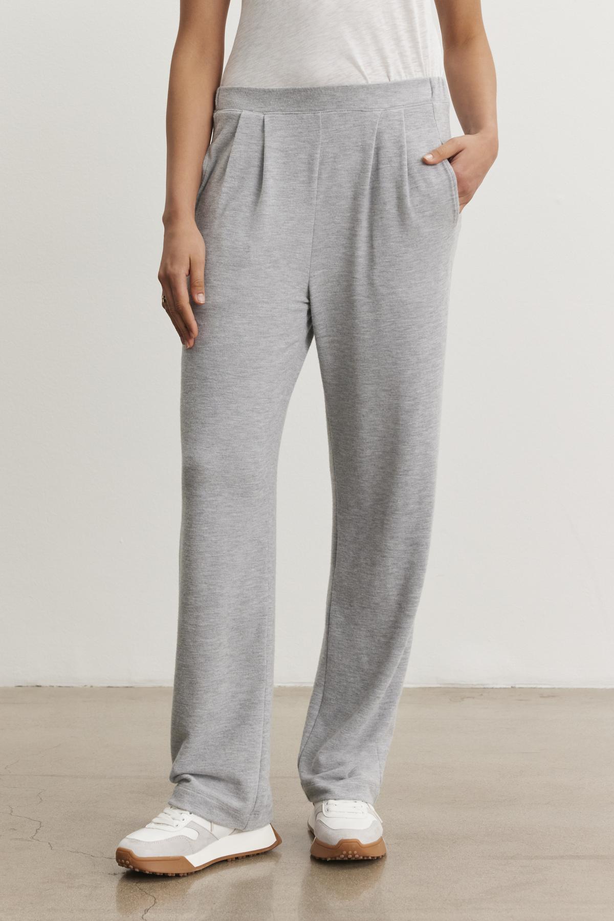Someone wearing Velvet by Graham & Spencer's ELIYA SWEATPANT in ultra-soft light gray triblend knit, paired with a white t-shirt and white sneakers, stands on a light floor against a plain wall.-38433293500609