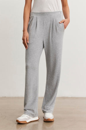 Someone wearing Velvet by Graham & Spencer's ELIYA SWEATPANT in ultra-soft light gray triblend knit, paired with a white t-shirt and white sneakers, stands on a light floor against a plain wall.