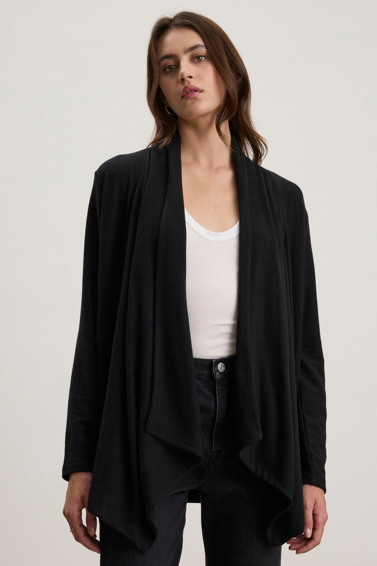 A person is wearing the Velvet by Graham & Spencer LISA CARDIGAN, a black triblend knit cardigan with an open front, over a white top and black pants, standing against a plain background.-38433284358337