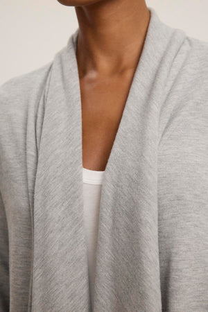 Close-up of a person wearing the LISA CARDIGAN from Velvet by Graham & Spencer over a white top. The luxurious triblend knit showcases an open front, with a soft, loose collar and side patch pockets.