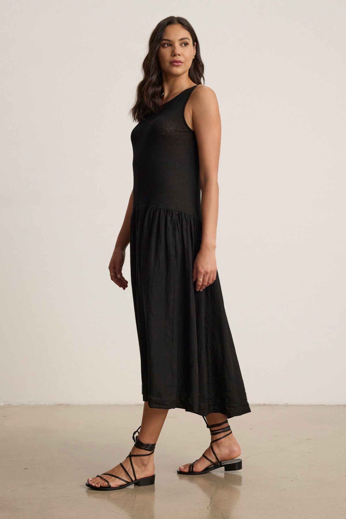 A woman stands indoors wearing the MABLE LINEN KNIT DRESS by Velvet by Graham & Spencer with black strappy sandals, her hair down as she looks slightly to the side.