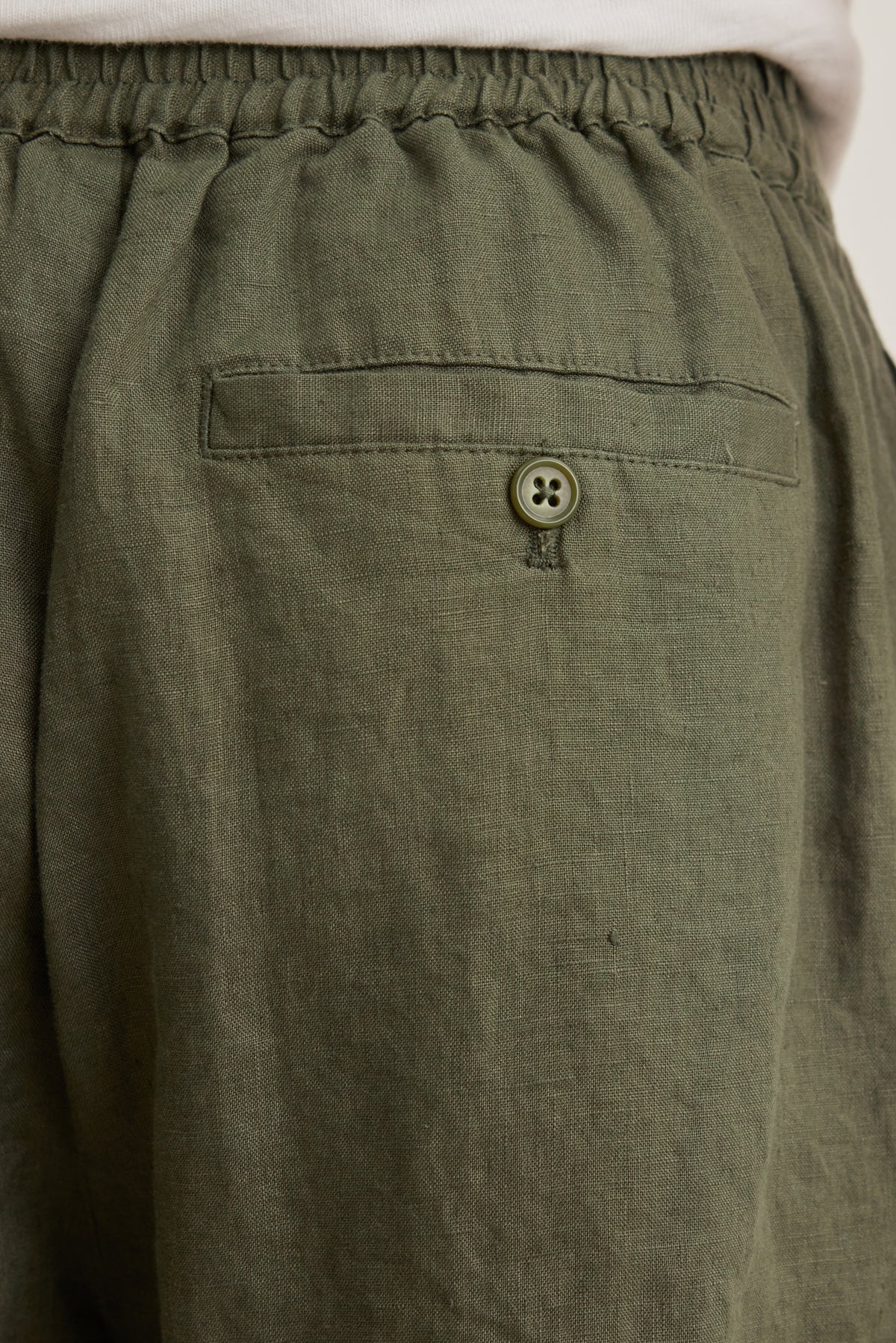 Close-up of the back pocket on the Velvet by Graham & Spencer EAMON LINEN SHORT in olive green; lightweight linen with an elastic waistband and a buttoned flap, ideal for warm weather and versatile style.