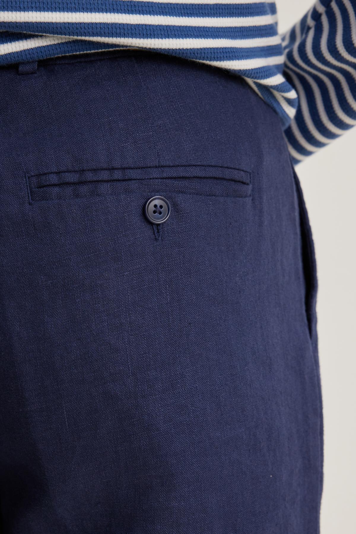 Close-up of a person wearing Velvet by Graham & Spencer's CANNON LINEN PANT with a single-buttoned pocket in navy, paired with a blue and white striped top.-38643234373825