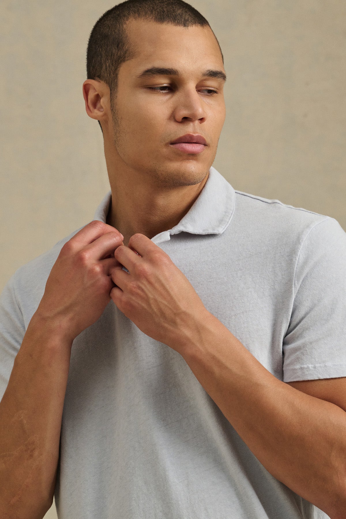 A man adjusts his collar and looks to the side, wearing the ASHTON POLO by Velvet by Graham & Spencer against a plain background.-41479914553537