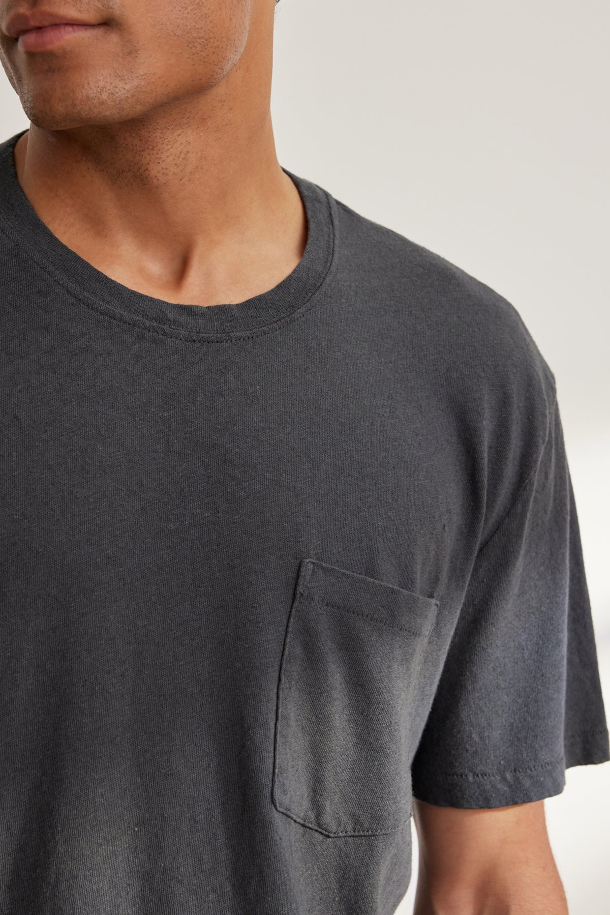 A man is shown from shoulders to mid-torso wearing the Velvet by Graham & Spencer LEVINSON LINEN COTTON TEE, a relaxed fit black crew neck premium tee with a chest pocket.-39096580767937