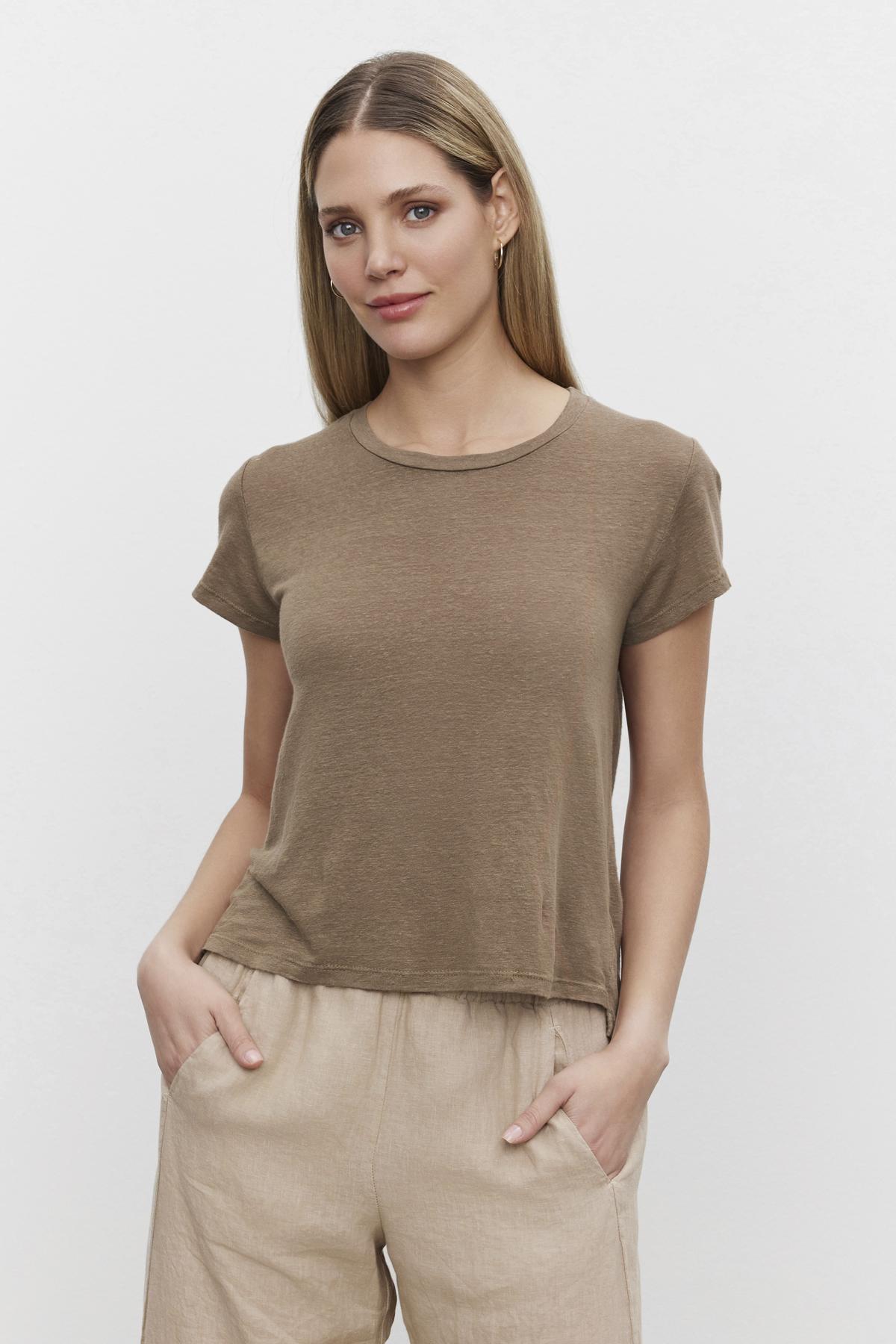   Woman wearing a Velvet by Graham & Spencer CASEY LINEN KNIT CREW NECK TEE and beige pants standing against a white background. 