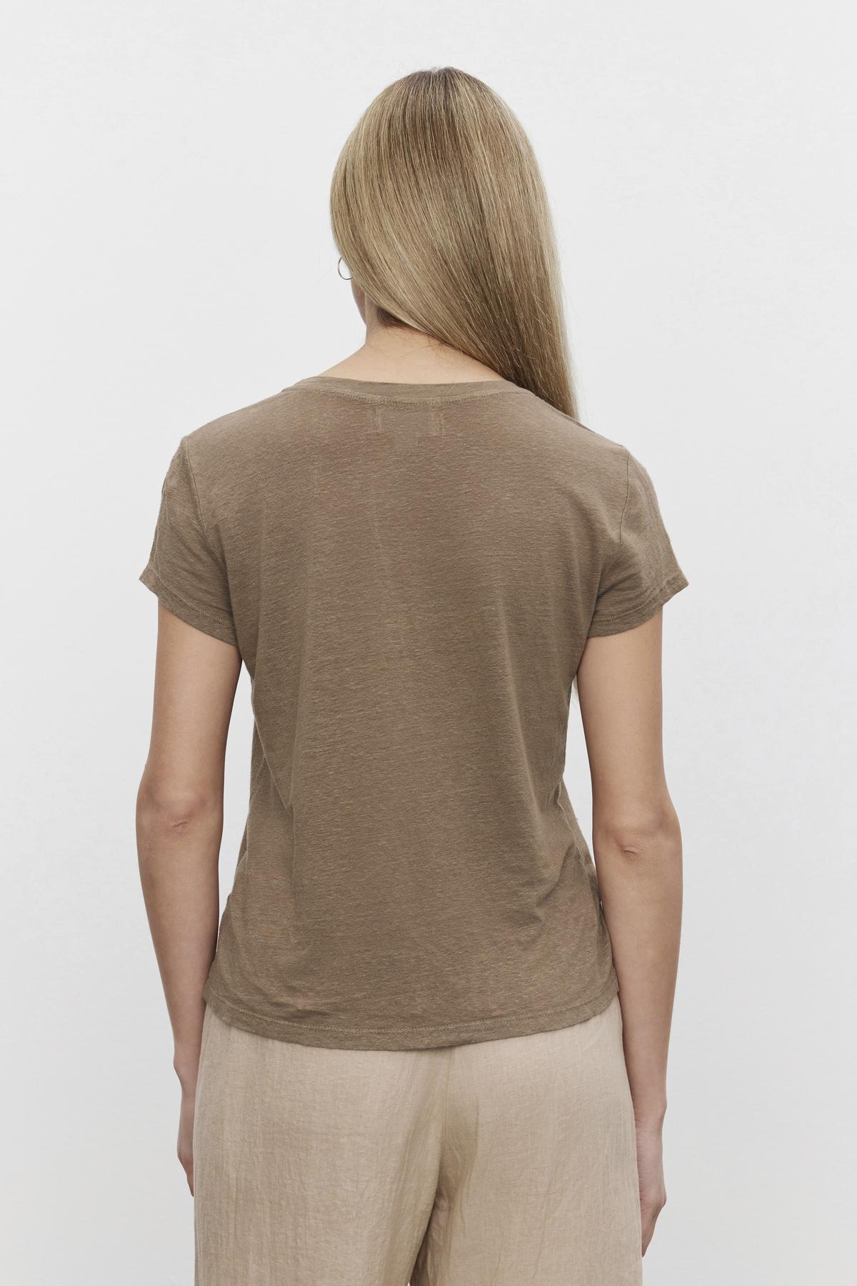   A woman seen from behind, wearing a Velvet by Graham & Spencer CASEY LINEN KNIT CREW NECK TEE with a hi-lo hemline and beige pants. 