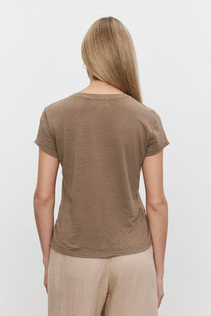 A woman seen from behind, wearing a Velvet by Graham & Spencer CASEY LINEN KNIT CREW NECK TEE with a hi-lo hemline and beige pants.