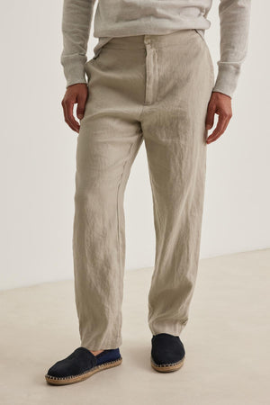 A person is wearing the LENNON LINEN PANT by Velvet by Graham & Spencer in beige, a light gray sweater, and black espadrilles.