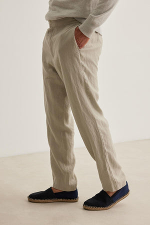 A person dressed in Velvet by Graham & Spencer's LENNON LINEN PANT and black espadrilles stands with hands in pockets against a white backdrop.