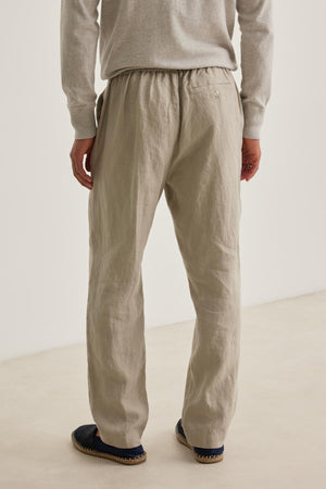 A person is seen from the back wearing a light grey long-sleeve shirt, dark loafers, and LENNON LINEN PANT by Velvet by Graham & Spencer in beige with a drawstring.