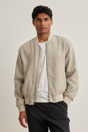 An individual wearing the Murphy Linen Bomber Jacket by Velvet by Graham & Spencer over a white shirt and dark pants stands against a plain background.