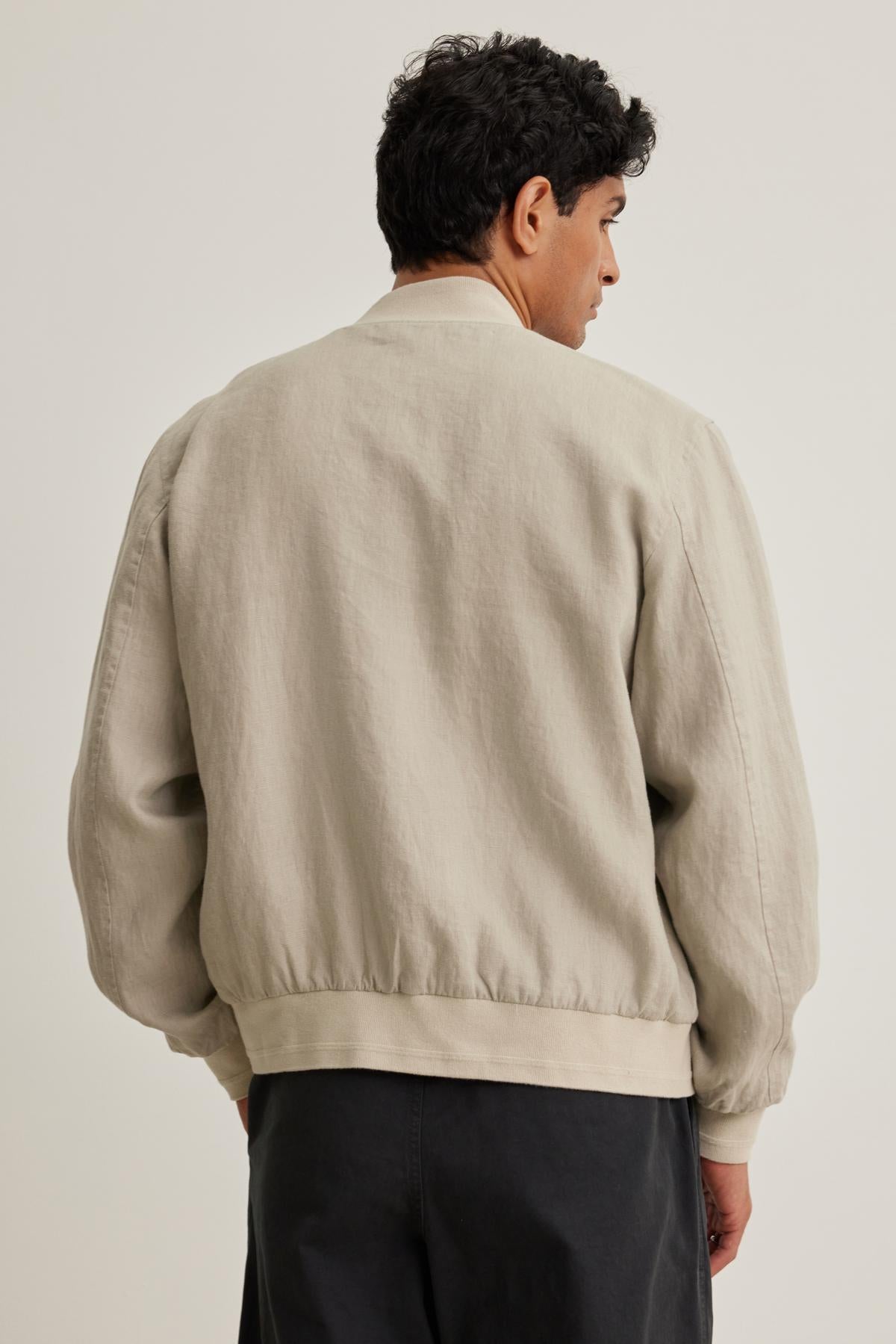 Individual wearing the MURPHY LINEN BOMBER JACKET by Velvet by Graham & Spencer with dark pants, facing away from the camera against a plain backdrop.-38643330449601