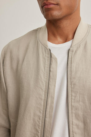 Someone wearing the MURPHY LINEN BOMBER JACKET by Velvet by Graham & Spencer over a white t-shirt, with a partial view of their face and shoulders.