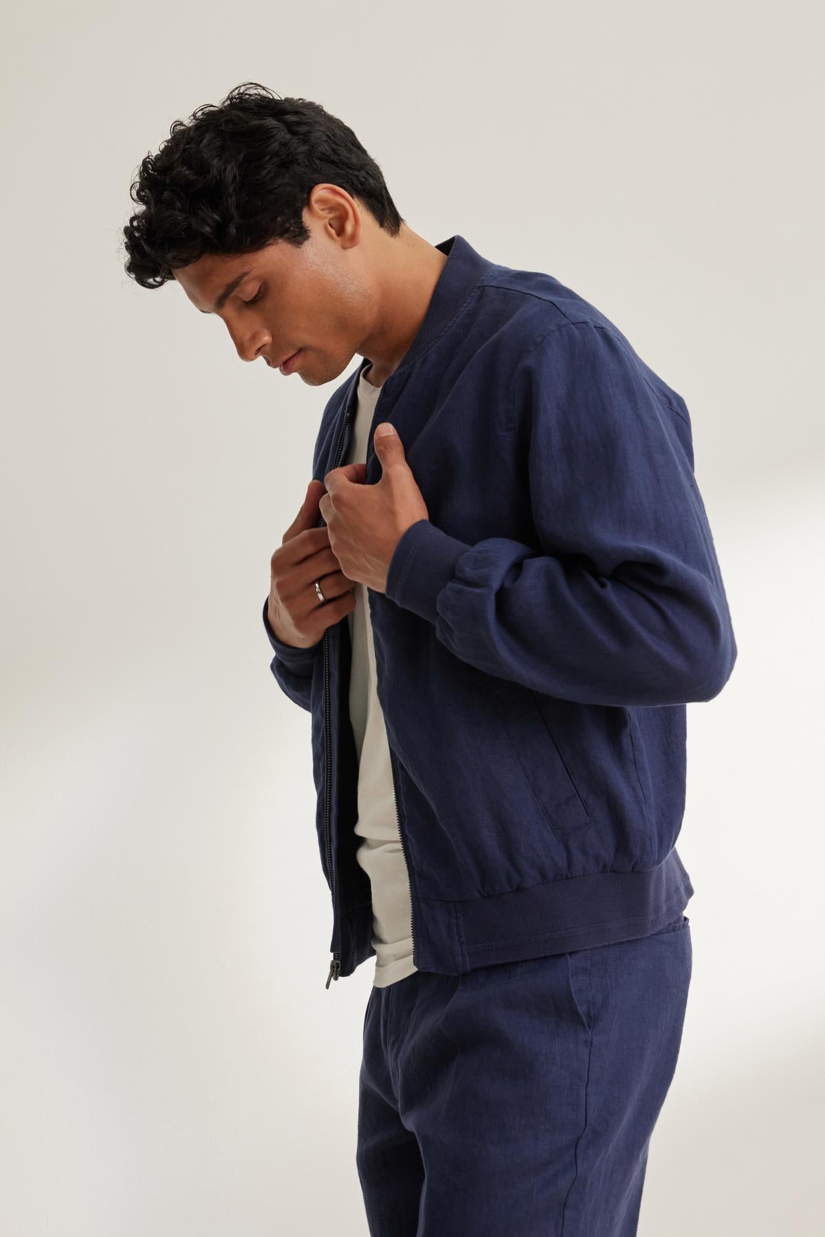 Person wearing the MURPHY LINEN BOMBER JACKET by Velvet by Graham & Spencer over a white shirt, looking down against a neutral background.-38643330711745