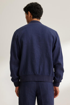 A person with short dark hair wearing a Velvet by Graham & Spencer Murphy Linen Bomber Jacket and dark pants is standing, facing away.