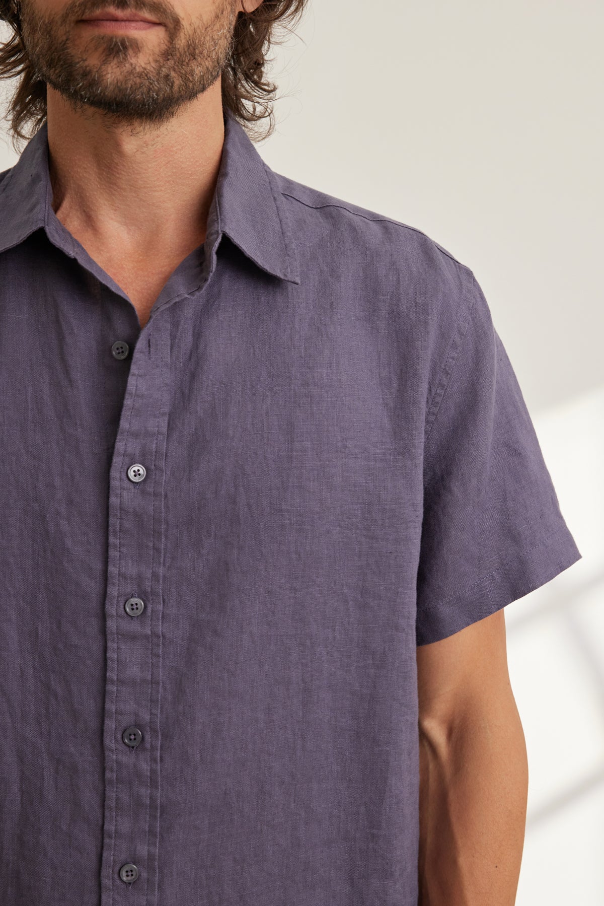 A man models the MICAH LINEN BUTTON-UP SHIRT by Velvet by Graham & Spencer—a short-sleeved, purple shirt in breathable linen—standing against a plain, light background to highlight its versatile style.-39096585748673