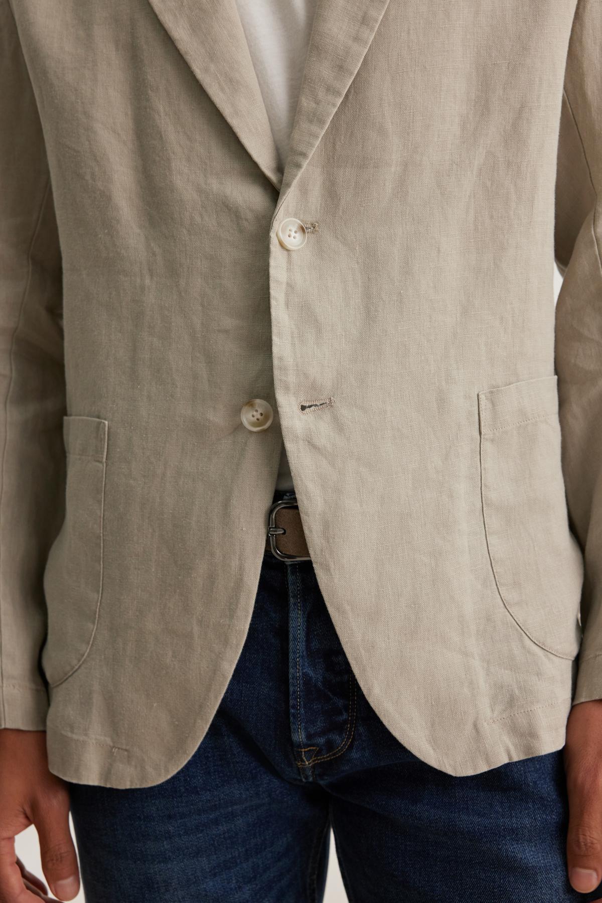 A person wearing the WARREN LINEN BLAZER by Velvet by Graham & Spencer over a white shirt and blue jeans, with hands partially visible in pockets.