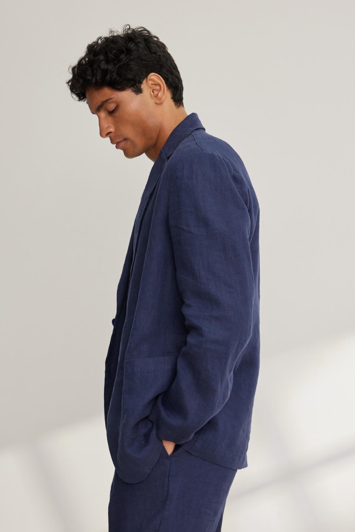 A person wearing the Velvet by Graham & Spencer WARREN LINEN BLAZER stands with hands in pockets against a light background.