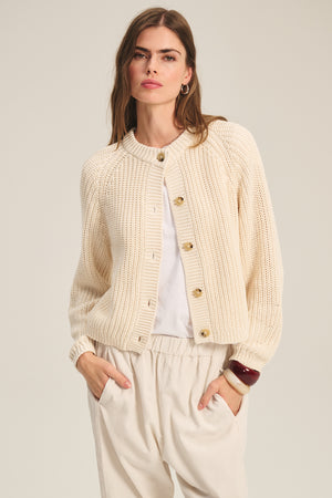 Model wears the LISABETH CARDIGAN by Velvet by Graham & Spencer, a chunky cropped layer with large buttons, styled over a white shirt and light beige pants—perfect for effortless transitional style.