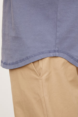 Close-up of a blue cotton knit DEON HENLEY shirt hem over beige trousers, focusing on the fabric and stitching detail by Velvet by Graham & Spencer.