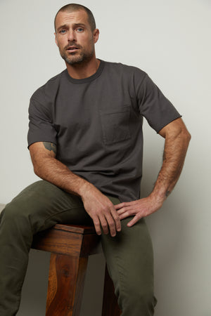 A man sitting on a stool in a Velvet by Graham & Spencer NEPTUNE CREW NECK POCKET TEE.