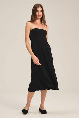 A woman stands against a plain background wearing the LUELLA SKIRT by Velvet by Graham & Spencer, styled in black with an elegant A-line silhouette and paired with matching black flats.