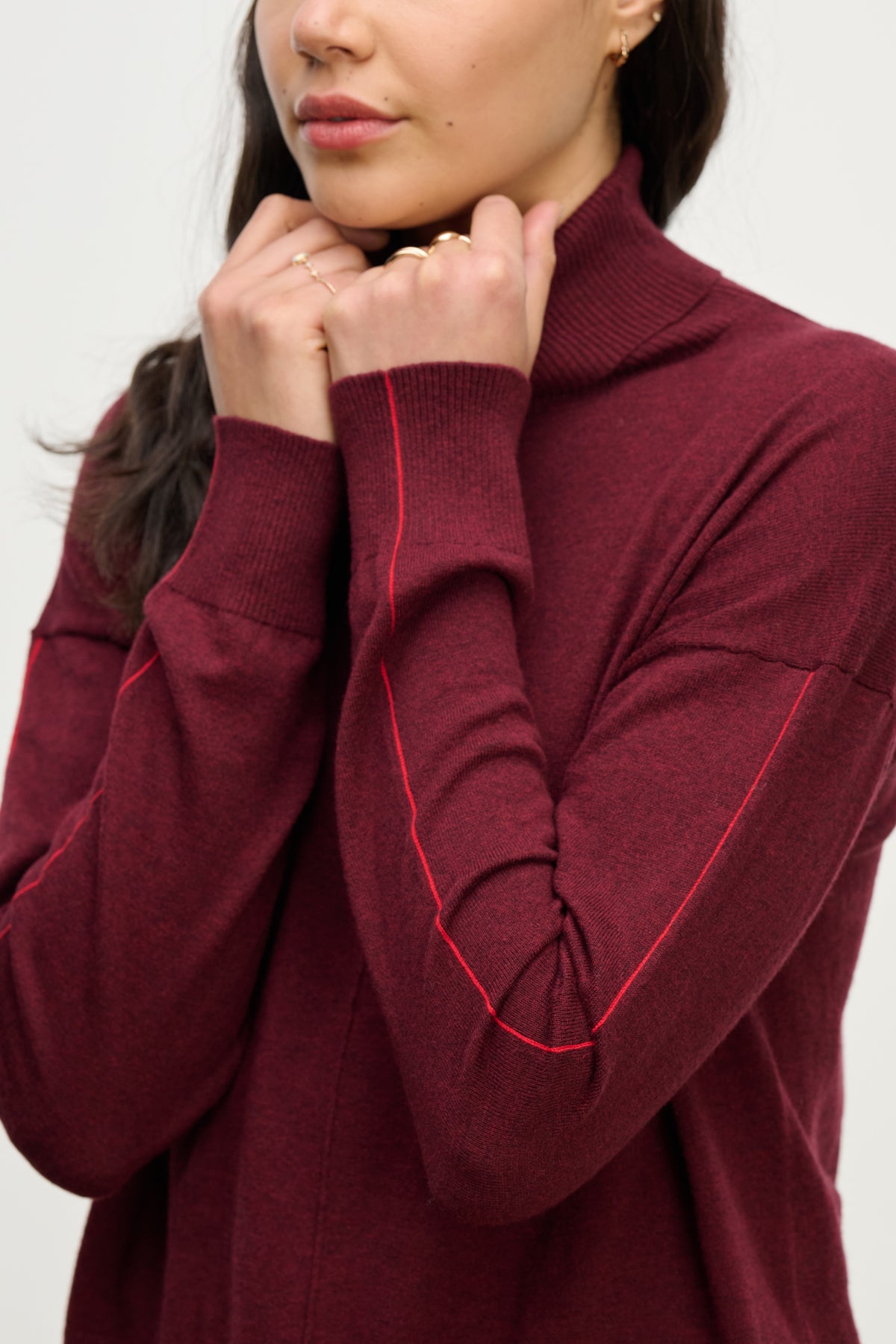 A woman wears the LIBRA SWEATER by Velvet by Graham & Spencer, a maroon cotton-cashmere turtleneck with long sleeves, standing with her hands near her chin.-40227068444865