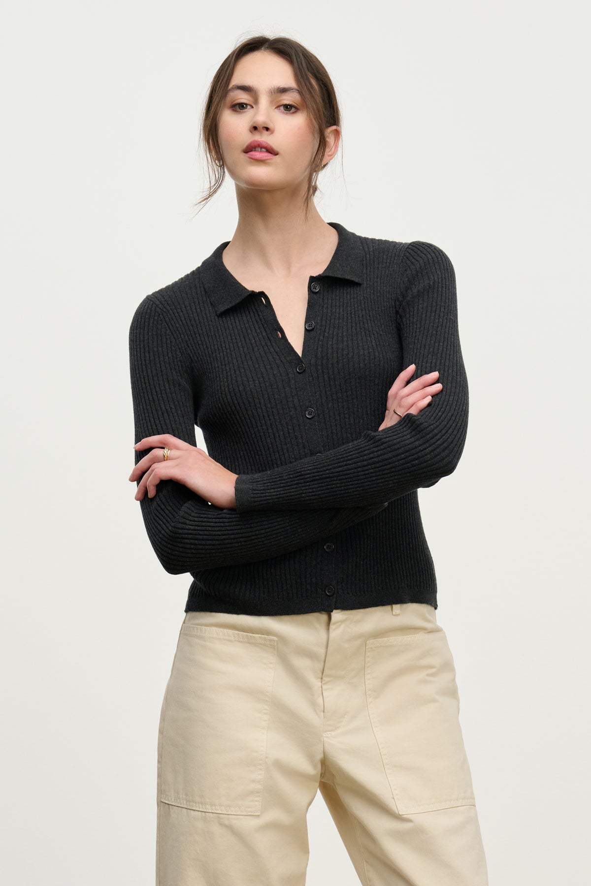 A woman stands with arms crossed, wearing the NIKKI COTTON CASHMERE CARDIGAN by Velvet by Graham & Spencer in black and light beige pants against a plain light background.