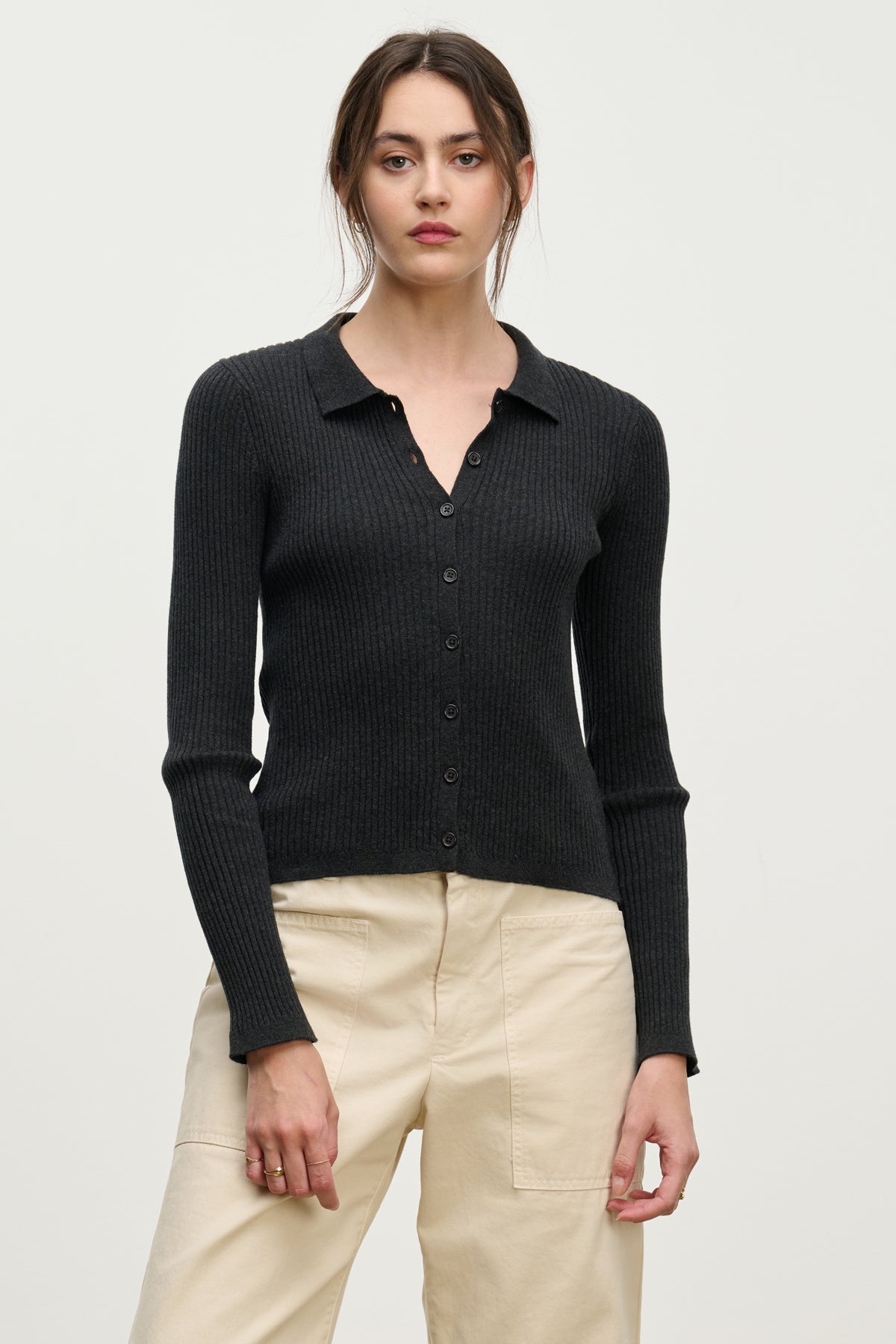 A woman models the NIKKI CARDIGAN by Velvet by Graham & Spencer—a black cotton cashmere cardigan with a collar—paired with beige high-waisted pants against a plain light background, highlighting this elegant layering piece.-39742357930177