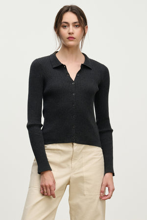 A woman models the NIKKI CARDIGAN by Velvet by Graham & Spencer—a black cotton cashmere cardigan with a collar—paired with beige high-waisted pants against a plain light background, highlighting this elegant layering piece.