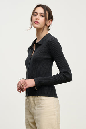 A person with long dark hair tied back models the NIKKI COTTON CASHMERE CARDIGAN by Velvet by Graham & Spencer, layered stylishly over light beige pants against a plain light background.