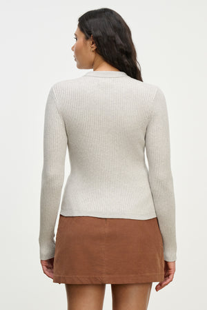 A woman with her back to the camera wears the Velvet by Graham & Spencer NIKKI COTTON CASHMERE CARDIGAN in light grey and a brown skirt, set against a plain background.