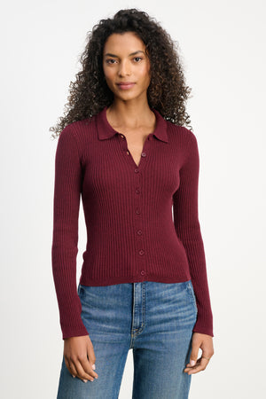 A woman with curly hair wears the Velvet by Graham & Spencer NIKKI Cotton Cashmere Cardigan in burgundy, styled with blue jeans, standing against a plain white background.