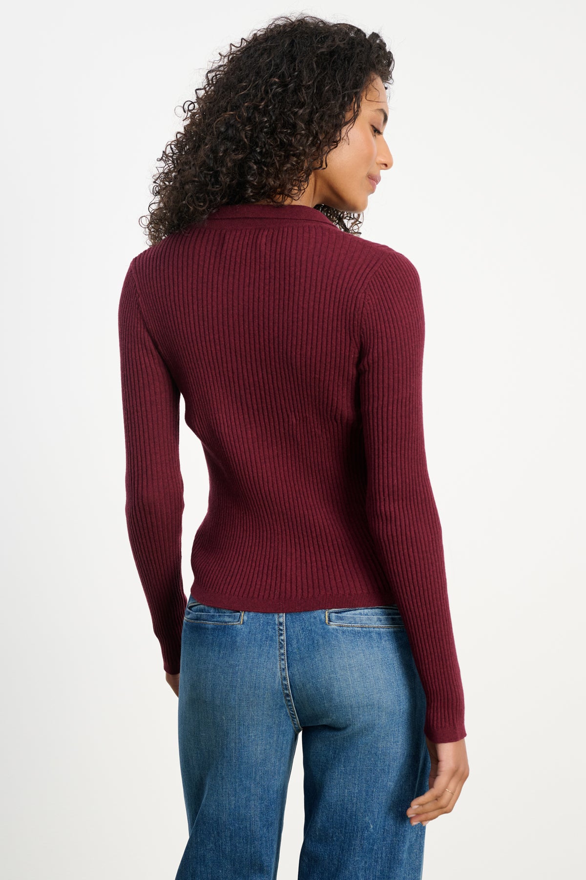 A person with curly hair is seen from behind wearing the Velvet by Graham & Spencer NIKKI Cotton Cashmere Cardigan in maroon, paired with blue jeans.