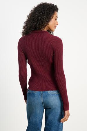 A person with curly hair is seen from behind wearing the Velvet by Graham & Spencer NIKKI Cotton Cashmere Cardigan in maroon, paired with blue jeans.