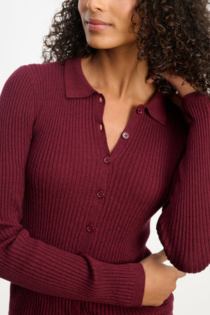 A woman models the Velvet by Graham & Spencer NIKKI COTTON CASHMERE CARDIGAN—a long-sleeve, ribbed, burgundy button-front style with a collar—posing with one hand in her hair.