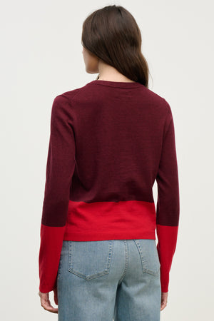 A person with long brown hair, seen from the back against a light background, wears blue jeans and a maroon-and-red ROXY SWEATER by Velvet by Graham & Spencer. The lightweight sweater adds comfort and style to the casual outfit.