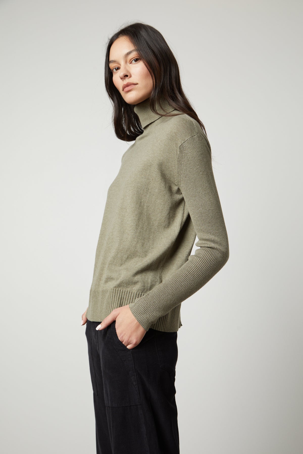 A model wearing a Velvet by Graham & Spencer ribbed green SALLY MOCK NECK SWEATER and fitted black trousers.-35503515959489
