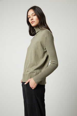 A model wearing a Velvet by Graham & Spencer ribbed green SALLY MOCK NECK SWEATER and fitted black trousers.