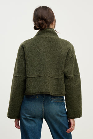 A person with brown hair in a low bun is seen from behind wearing Velvet by Graham & Spencer's KELLY LUXE SHERPA REVERSIBLE JACKET in olive green and blue jeans, set against a plain background.