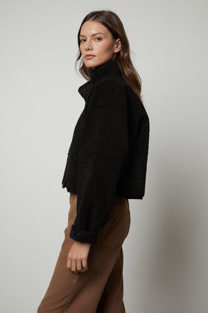 The model is wearing a black KELLY LUX SHERPA REVERSIBLE JACKET by Velvet by Graham & Spencer and brown pants.
