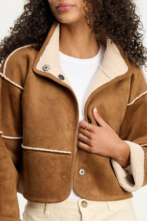 A woman wearing the KELLY LUXE SHERPA REVERSIBLE JACKET by Velvet by Graham & Spencer over a white shirt and cream pants, holding one jacket lapel.