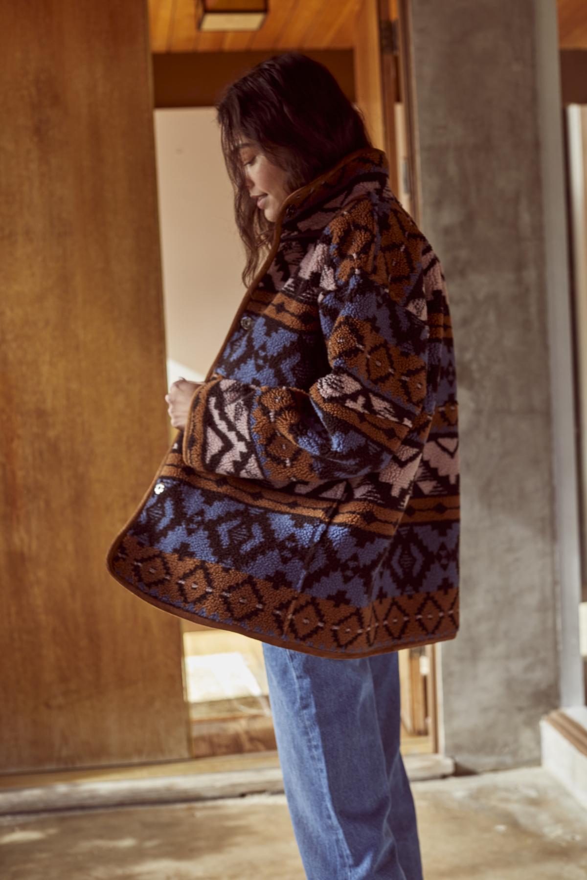 A woman wearing a Velvet by Graham & Spencer LAILA PRINTED SHERPA REVERSIBLE JACKET and jeans standing in front of a door.-26905633849537