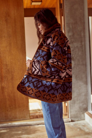 A woman wearing a Velvet by Graham & Spencer LAILA PRINTED SHERPA REVERSIBLE JACKET and jeans standing in front of a door.