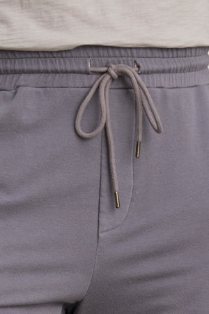 Close-up of a person wearing the Velvet by Graham & Spencer CROSBY JOGGER in light gray luxe fleece with a drawstring, paired with a white shirt.