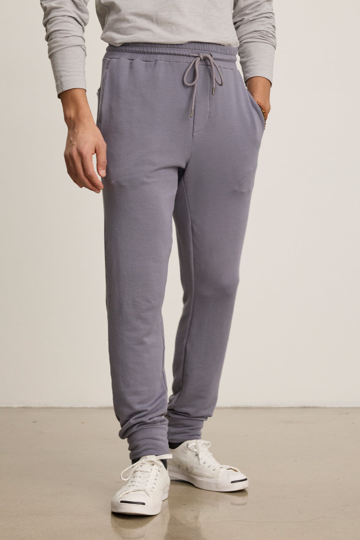 A person wearing the CROSBY JOGGER by Velvet by Graham & Spencer, paired with a light gray long-sleeve shirt and white sneakers, stands on a polished floor against a plain background.